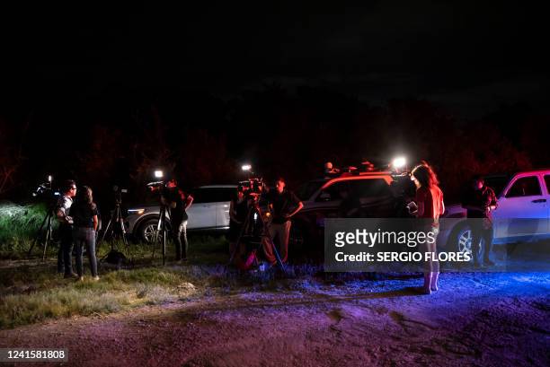 News reporters stand near the scene where a tractor-trailer was discovered with migrants inside outside San Antonio, Texas on June 27, 2022. At least...