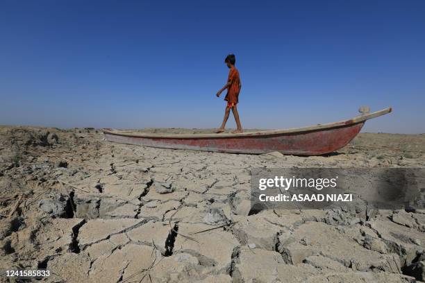 Boy walks on a boat left lying on the dried-up bed of a section of Iraq's receding southern marshes of Chibayish in Dhi Qar province, on June 28,...