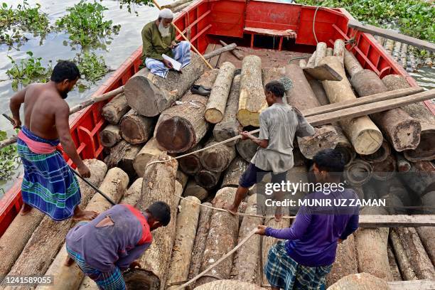 Labourers unload logs of wood from a boat in Buriganga river in Dhaka on June 28, 2022.