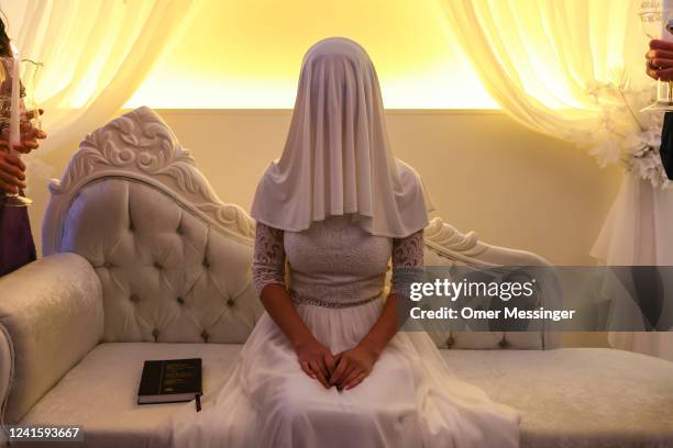 Bride Elisheva Chayaa sits with a veil covering her face as she is surrounded by family members during a Jewish marriage ceremony held by Chabad...