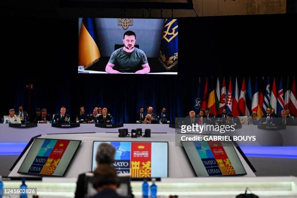 Ukraine's President Volodymyr Zelensky appears on a giant screen as he delivers a statement at the start of the first plenary session of the NATO...
