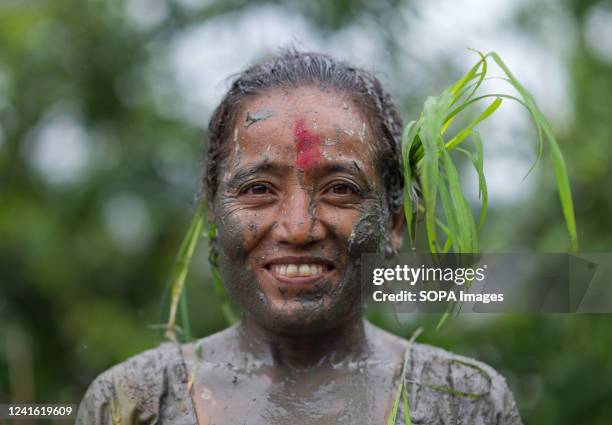 Woman covered in mud smiles in a rice paddy field during National Paddy Day celebration. Nepalese farmers celebrate National Paddy Day with various...