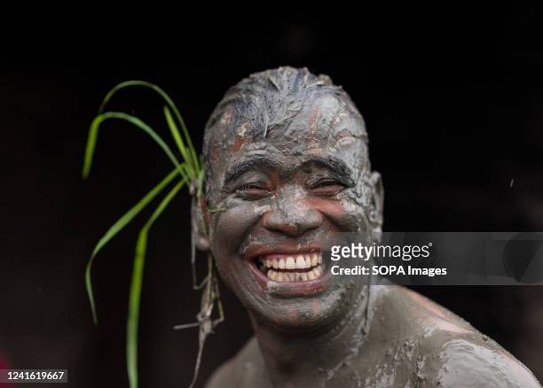 Man's face covered with mud smiles in a rice paddy field during the National Paddy Day. Nepalese farmers celebrate National Paddy Day with various...