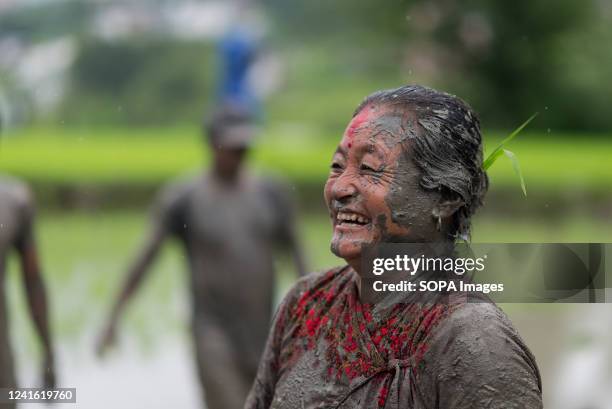 Woman covered in mud smiles in a rice paddy field during National Paddy Day celebration. Nepalese farmers celebrate National Paddy Day with various...