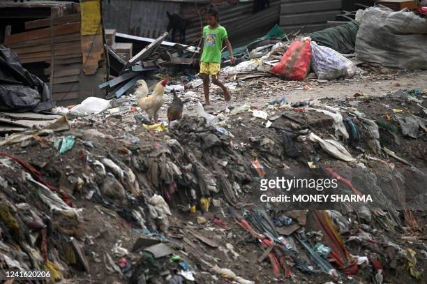 Girl walks past plastics and other waste dumped near a sewer canal in New Delhi on June 30, 2022. India imposed a ban on many single-use plastics on...