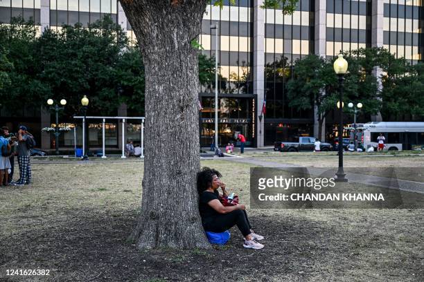 Migrant sits under a tree at a park near a shelter in San Antonio, Texas on June 29, 2022. - Dozens of migrants wait in line outside a shelter in San...