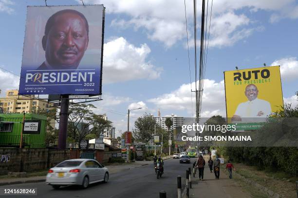 Pedestrians and motorists are seen next to campaign posters for Presidential candidates for Azimio La Umoja Raila Odinga and United Democratic...