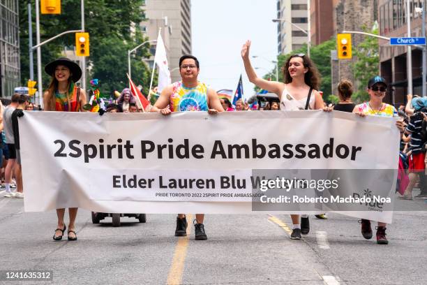 Group of people holding a banner announcing the 2Spirit Pride Ambassador Elder Lauren Blue Waters. They are marching in Bloor Street during Pride...