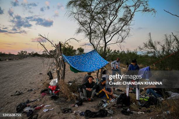 Migrants rest after crossing the Rio Grande River as they wait to get apprehended by Border Patrol agents as National Guard agents sit on a car...