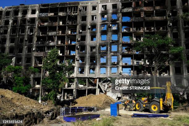 Workers get ready to dig in front of a destroyed building in the city of Mariupol on July 1 amid the ongoing Russian military action in Ukraine.