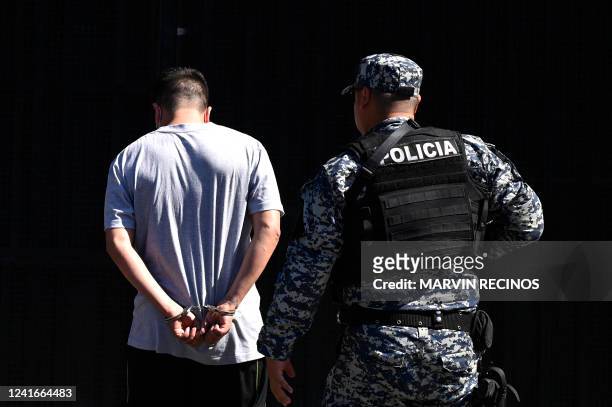 Man arrested for alleged gang links is escorted by an officer of the National Civil Police during the state of emergency declared by the Salvadoran...