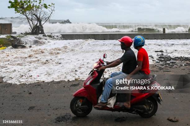 People ride a scooter along a road as waves crash over the promenade during monsoon winds in Galle on July 2, 2022.