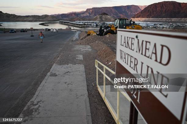 Visitor walks up a boat launch ramp that was recently extended to compensate for lower water levels as a sign indicates the 2021 Lake Mead Water Line...