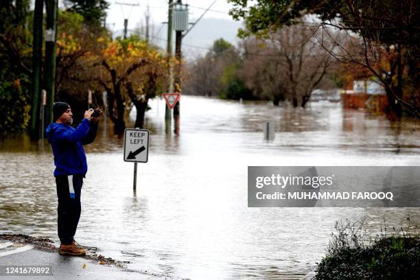 Man takes pictures of the flooded streets due to torrential rain in the Camden suburb of Sydney on July 3, 2022. Thousands of Australians were...