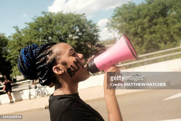 Woman with a Black Lives Matter sign painted on her face, speaks into a megaphone as demonstrators gather outside Akron City Hall to protest the...