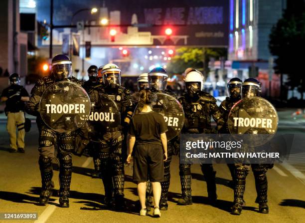Woman stands in front of troopers in riot gear as police deployed tear gas and stun grenades to clear the area around Akron City Hall and Akron...