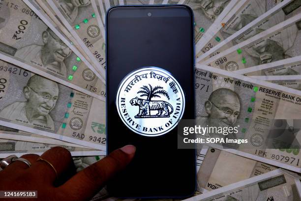 In this photo illustration, a Reserve bank of India logo is displayed on a smartphone screen with Indian Currency note illustrations in the...