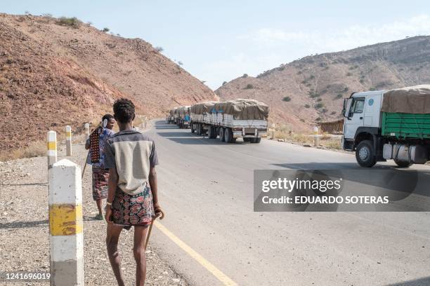 Men walk next to a convoy of trucks part of the World Food Programme on their way to Tigray in the village of Erebti, Ethiopia, on June 9, 2022. -...