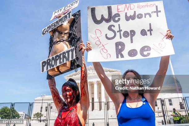 Abortion-rights supporter Sam Scarcello and anti-abortion activist Elianna Geertgens hold competing signs in front of the Supreme Court while covered...