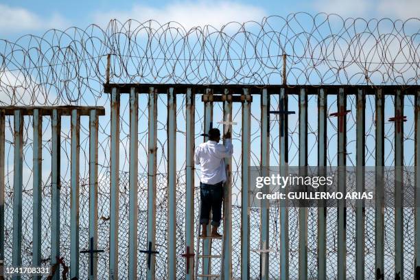 Josue Serrano, a Mexican deported migrant, hangs wooden crosses on the border fence as part of a vigil for migrants who died while migrating to the...
