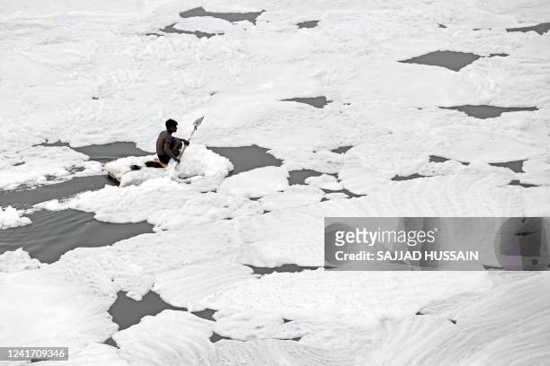 Man paddles his raft while collecting recyclable materials in the waters of river Yamuna coated with polluted foam in New Delhi on July 5, 2022.