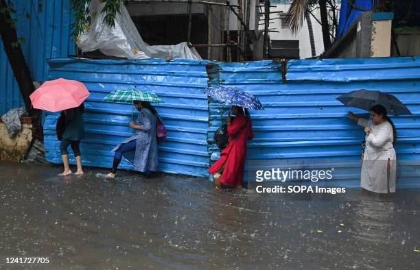 Women holding umbrellas are crossing a flooded street amidst heavy rain in Mumbai. Mumbai experienced flooded streets in low-lying areas, and traffic...