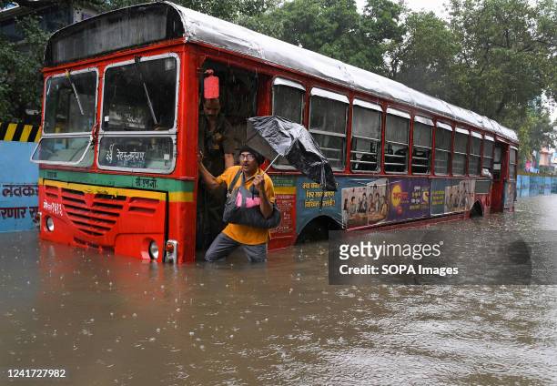 Man holding an umbrella alights from a BEST bus stranded on a flooded street amidst heavy rain in Mumbai. Mumbai experienced flooded streets in...