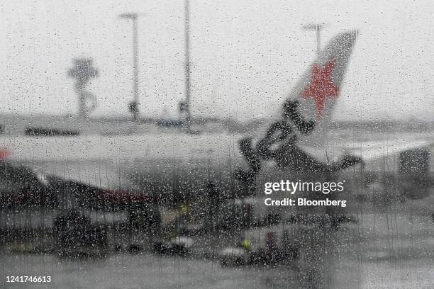 Rain droplets on a window near an aircraft operated by Qantas Airways Ltd.'s low-cost unit Jetstar Airways on the tarmac at Sydney Airport in Sydney,...