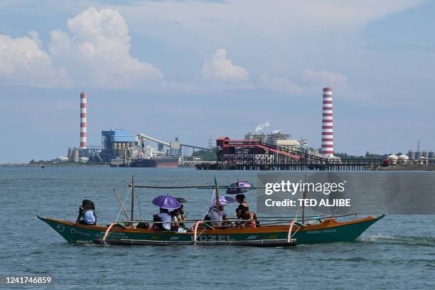 This photo taken on July 6, 2022 shows a coal fired power plant as people ride past on a wooden boat in Oyon Bay in Masinloc town, Zambales province.