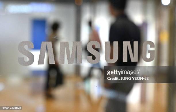 People walk past the Samsung logo displayed on a glass door at the company's Seocho building in Seoul on July 7, 2022.