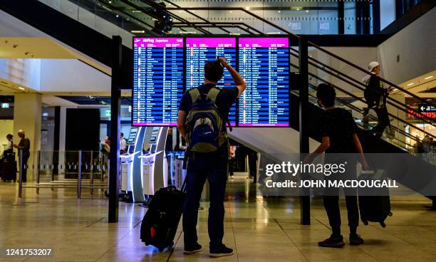 Passenger pauses in front of a digital billboard displaying flight information at Berlin Brandenburg International airport's terminal 1 near...