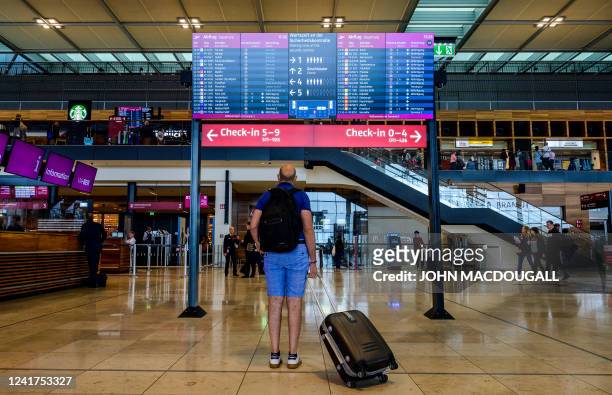 Passenger pauses in front of a digital billboard displaying flight information at Berlin Brandenburg International airport's terminal 1 near...