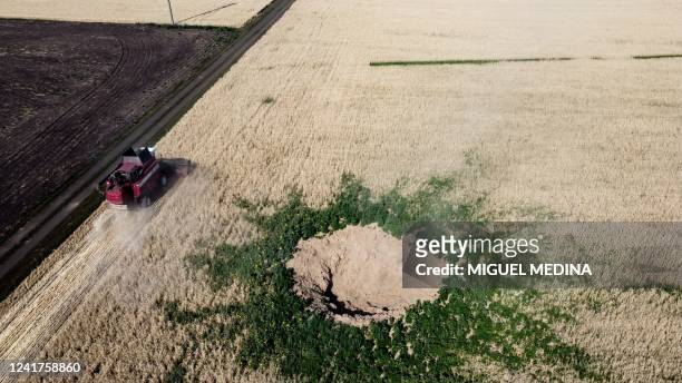 This aerial photograph taken on July 7 near Kramatorsk shows a farmer harvesting wheat as he drives a combine harvester near a crater suspected to be...