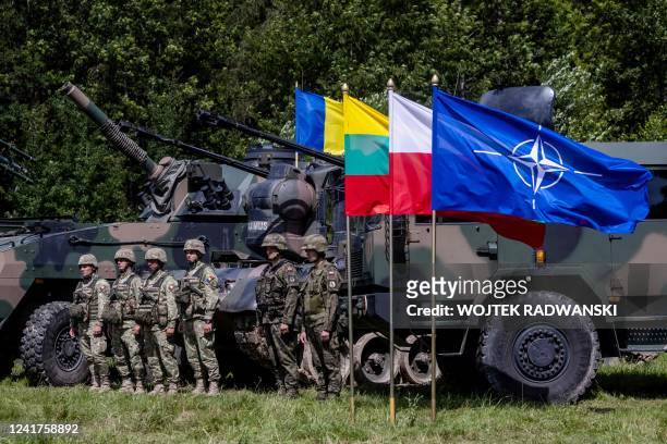 Polish and Romanian soldiers stand next to military vehicles and a NATO flag on the sidelines of a press conference of the Polish and Lithuanian...