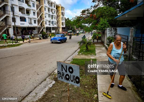 Woman sweeps the sidewalk in front of her house in La Guinera neighbourhood, on the outskirts of Havana, on June 30, 2022. - As Cuba marks the first...