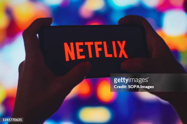 In this photo illustration, a silhouetted woman holds a smartphone with the Netflix logo displayed on the screen.