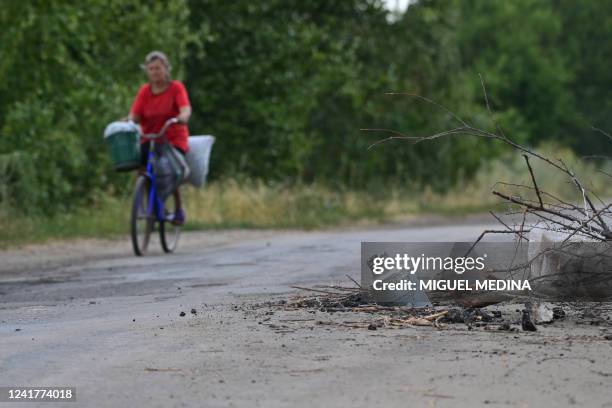Woman rides her bike next to a Russian rocket half sunk in the middle of the street near Siversk, in Donetsk Oblast, eastern Ukraine, on July 8 amid...