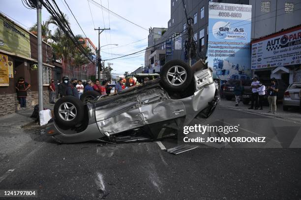 People stand next to a car after it dumped and a person was taken to a local hospital, in Guatemala City, on July 9, 2022. - According to a report of...