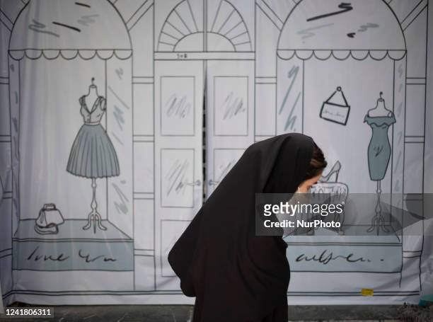 An Iranian woman walks past a shop window covered with a banner in northern Tehran on July 9, 2022. Iranian President Ebrahim Raisi called in a...
