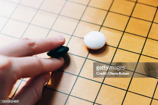 hand holds stone for playing go to the white game stone - go board game stock pictures, royalty-free photos & images