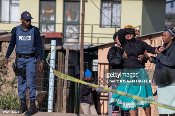 Relative of one of the victims cries as south African Police Service officers refuse to let her cross the police barrier and enter the crime scene in...