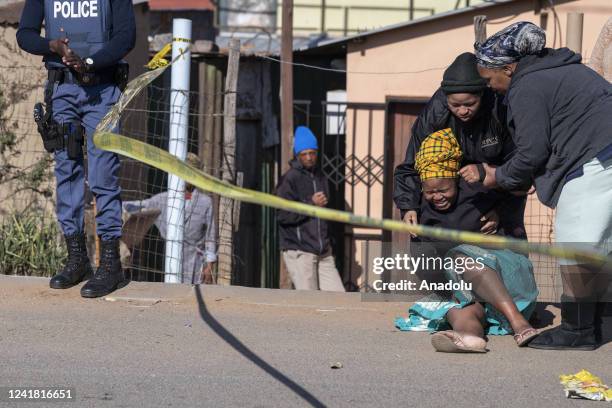 Woman reacts as securtiy forces and forensic service inspect the scene of a mass shooting in Soweto, South Africa, on July 10, 2022. Fourteen people...