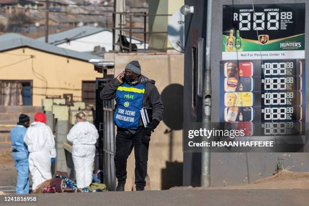 South African Police Service crime scene investigator talks on his phone at the scene of a mass shooting in Soweto, South Africa, on July 10, 2022. -...