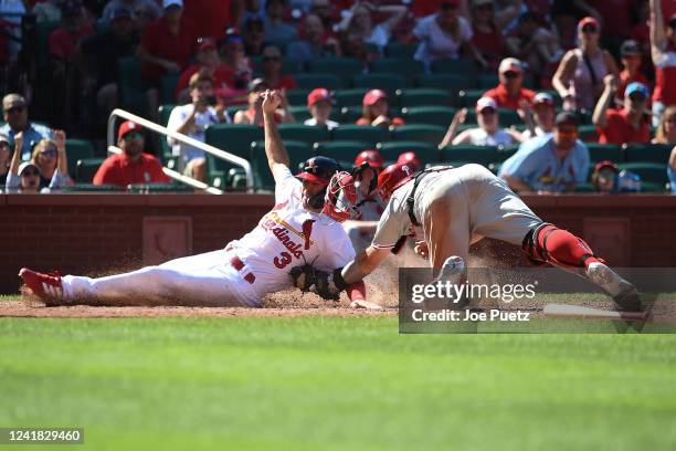 Dylan Carlson of the St. Louis Cardinals is safe at home plate ahead of the tag from J.T. Realmuto of the Philadelphia Phillies at Busch Stadium on...