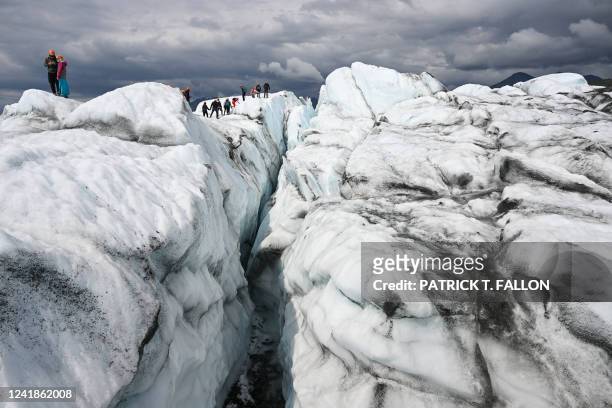 Visitors hike on the ice along a crevasse during a guided tour on the Matanuska Glacier, a 27-mile long valley glacier feeding water into the...