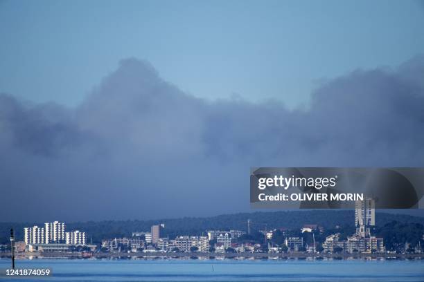 Firefighter airplane flies over a plume of dark smoke, due to a wildfire in a forest near Teste-de-Buch as seen from the shoreline of Arcachon, in...