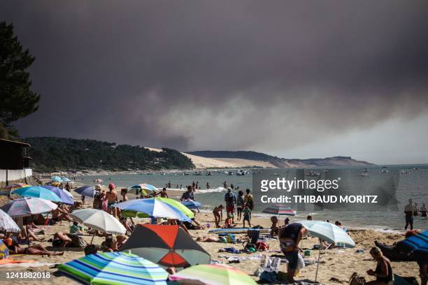 Beach-goers bathe and lay at a beach of "Pyla sur mer" as a black cloud of smoke from a fire that hit La Teste-de-Buch forest rises from the Dune of...