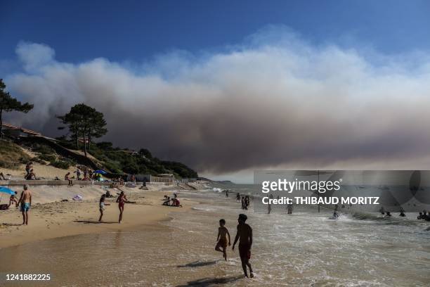 Beach-goers bathe and lay at a beach of "Pyla sur mer" as a black cloud of smoke from a fire that hit La Teste-de-Buch forest rises from the Pyla...