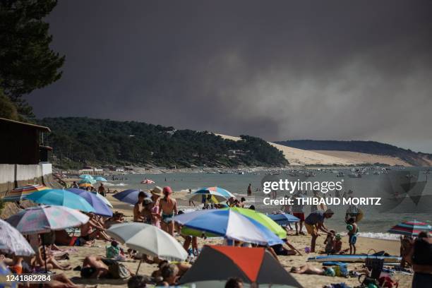 Beach-goers bathe and lay at a beach of "Pyla sur mer" as a black cloud of smoke from a fire that hit La Teste-de-Buch forest rises from the Dune of...