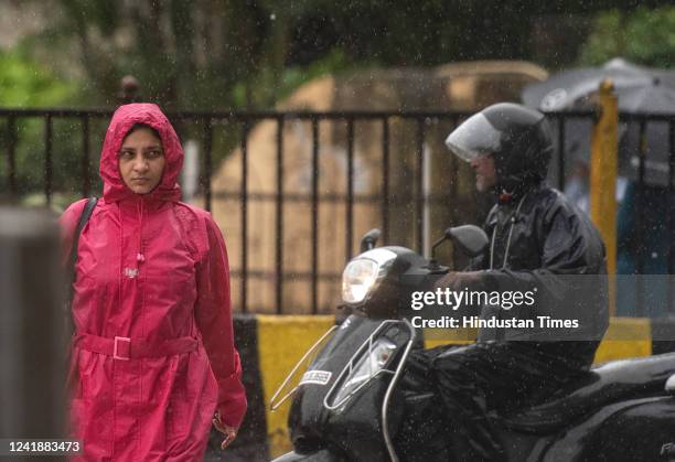 Woman crosses the road while a scooterist rides through heavy rain near Churchgate station on July 13, 2022 in Mumbai, India. The India...